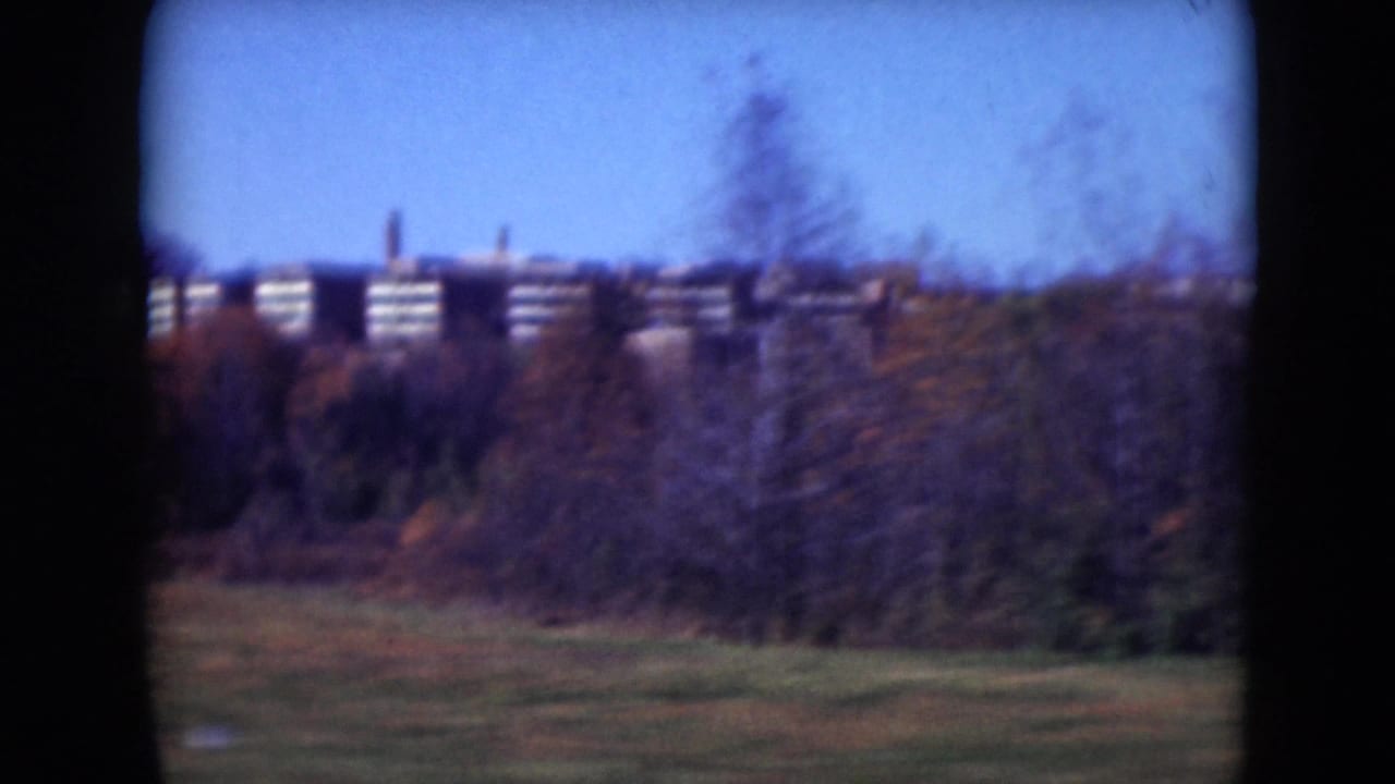 Roadside Middletown landscape with autumn brush, grass, blue sky, and distant brick buildings viewed from inside a moving vehicle.