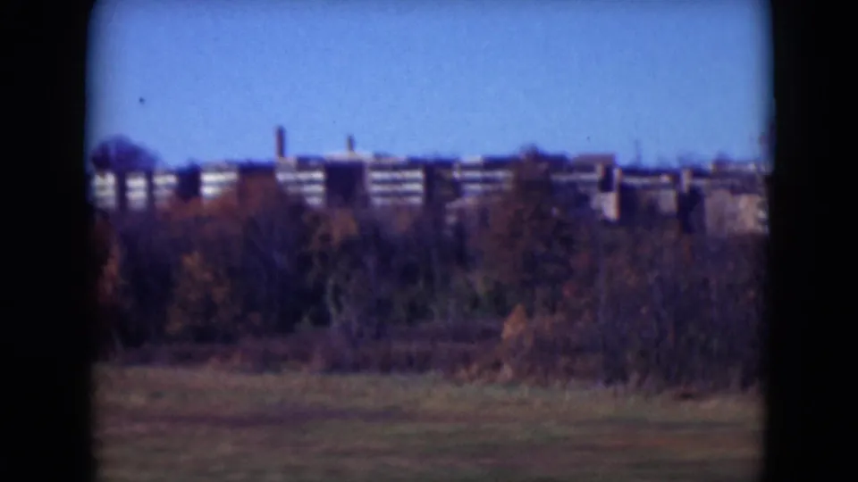 1975 Middletown view across grass and fall foliage toward a long brick building complex with repeated window bands.