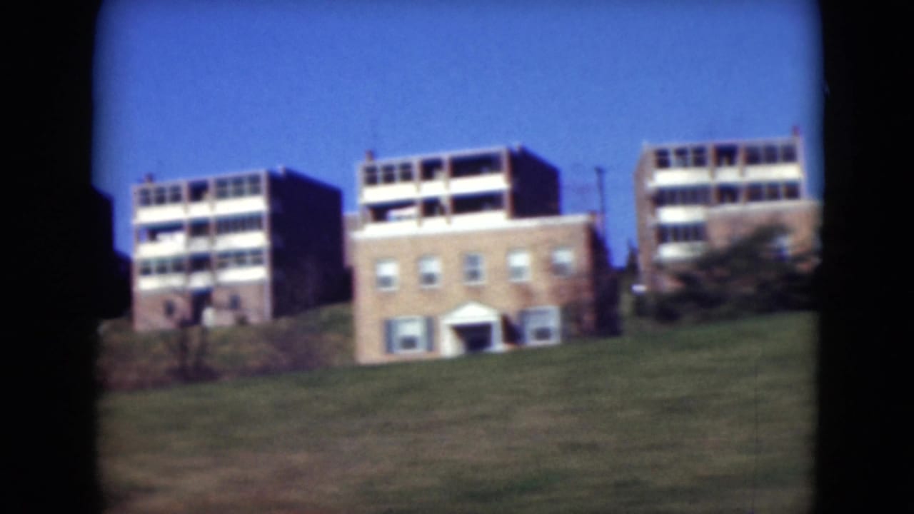 1975 Middletown, Pennsylvania view of mid-century apartment buildings on a grassy slope, filmed from a passing vehicle.