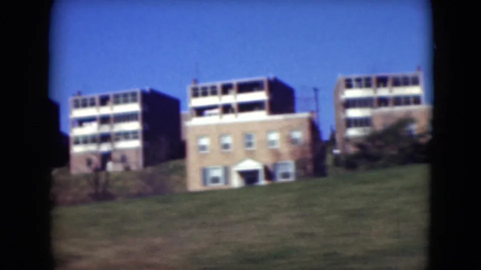 1975 Middletown, Pennsylvania view of mid-century apartment buildings on a grassy slope, filmed from a passing vehicle.