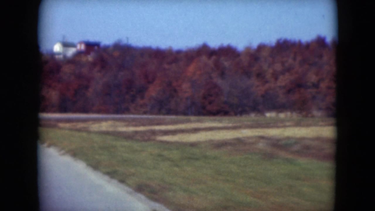 Passing 1975 Middletown-area road view with fields, autumn woods, and a few distant houses on the ridge.