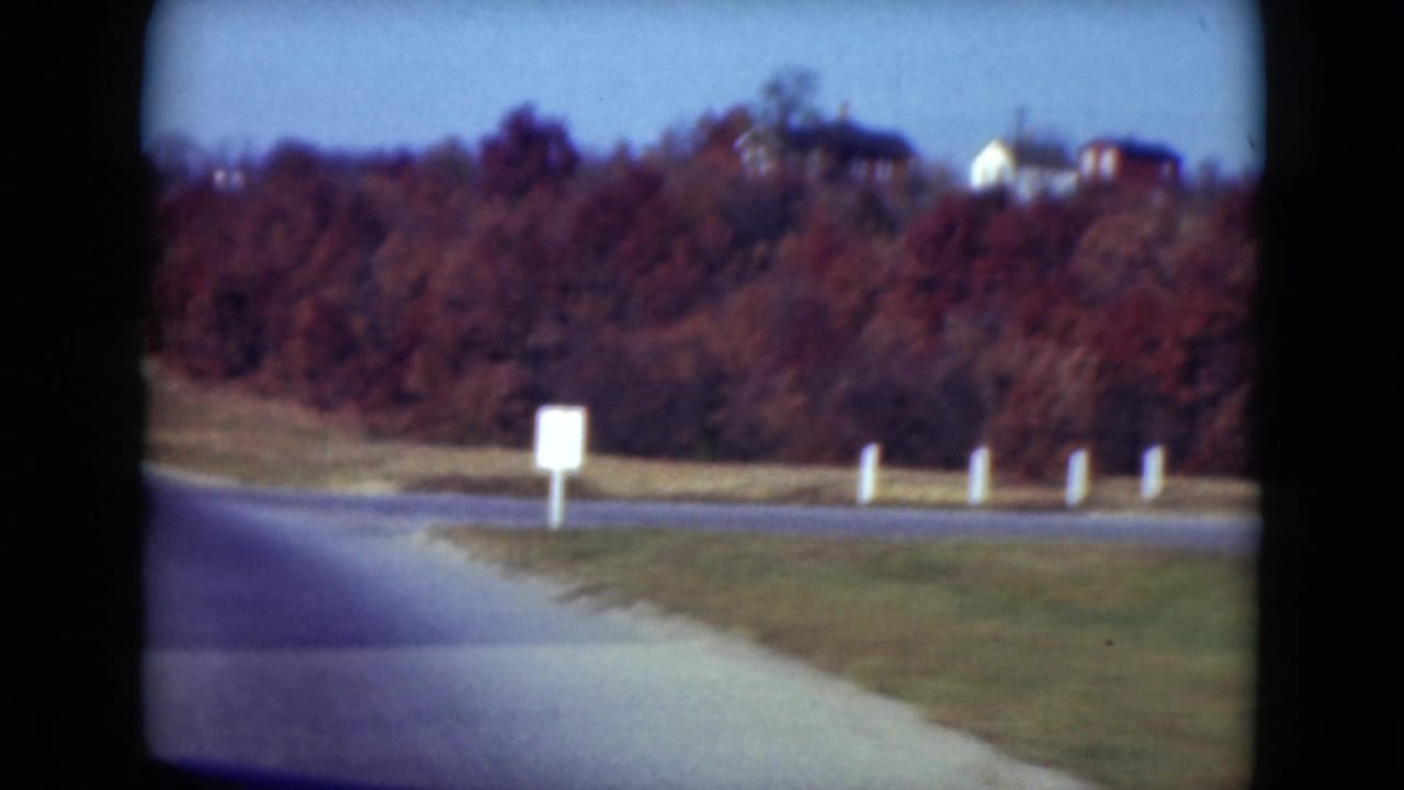 Curving road beside grass and autumn trees with distant hillside houses.