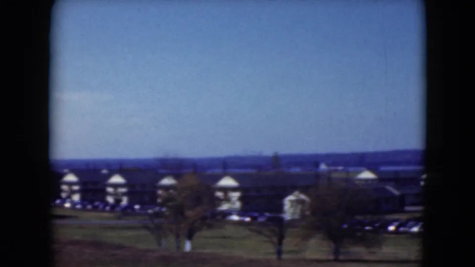Wide 1975 Middletown view showing low rounded-roof buildings, scattered trees, parked cars, and distant hills beneath a clear sky.
