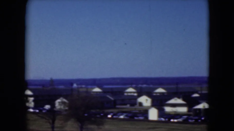 Distant Middletown landscape with a row of low buildings, rounded roofs, parked cars, open grass, and a blue 8mm sky.