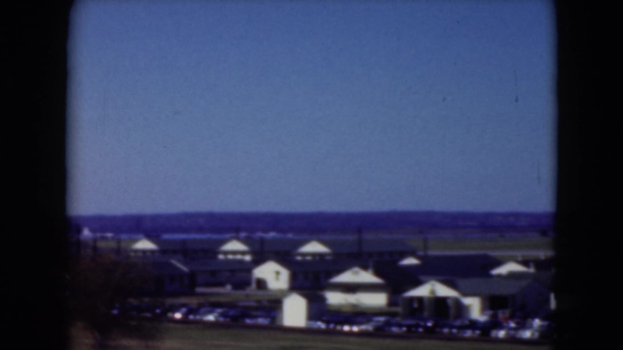 1975 Middletown, Pennsylvania home-movie view of low waterfront buildings, a parking area, water, and open sky.