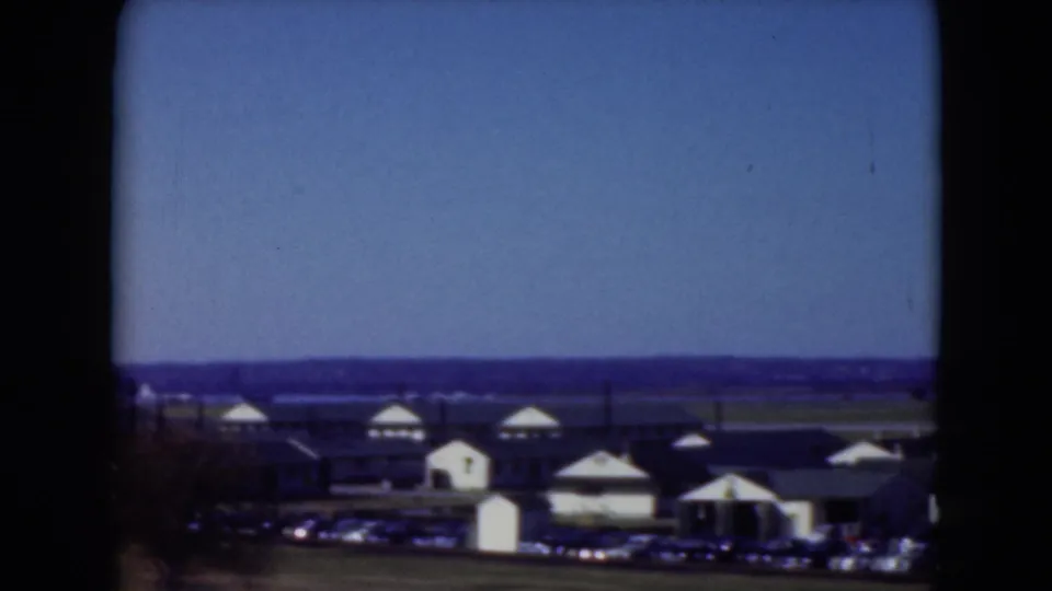 1975 Middletown, Pennsylvania home-movie view of low waterfront buildings, a parking area, water, and open sky.