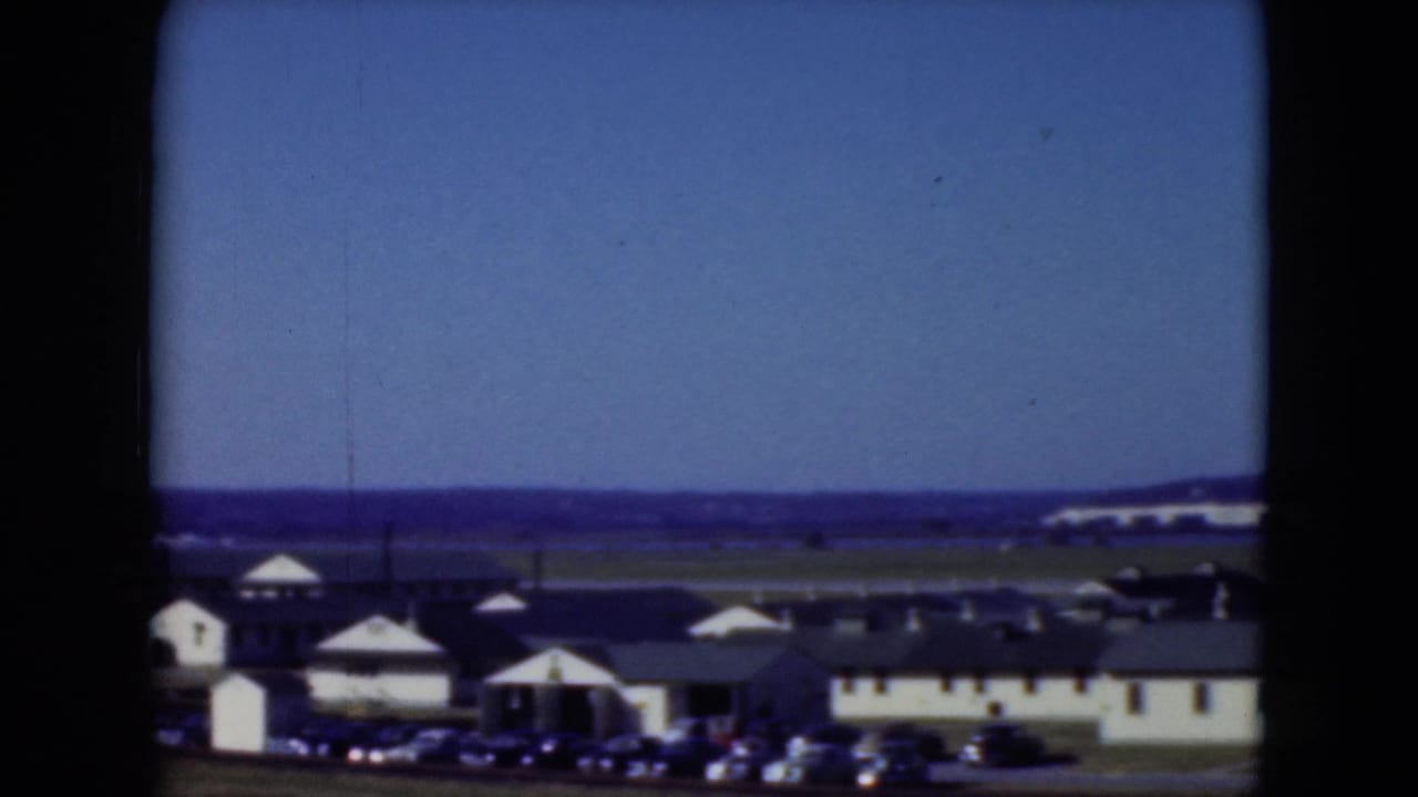 A 1975 home-movie frame shows Middletown waterfront buildings and parked cars beneath a clear sky.