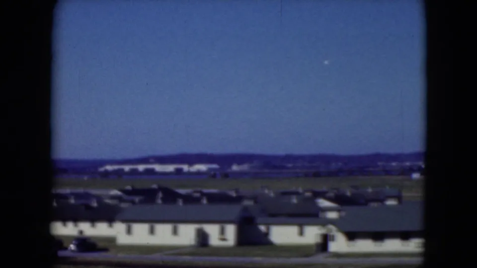 Final 1975 Middletown frame showing a low waterfront structure, cars, open sky, and distant water or shoreline.