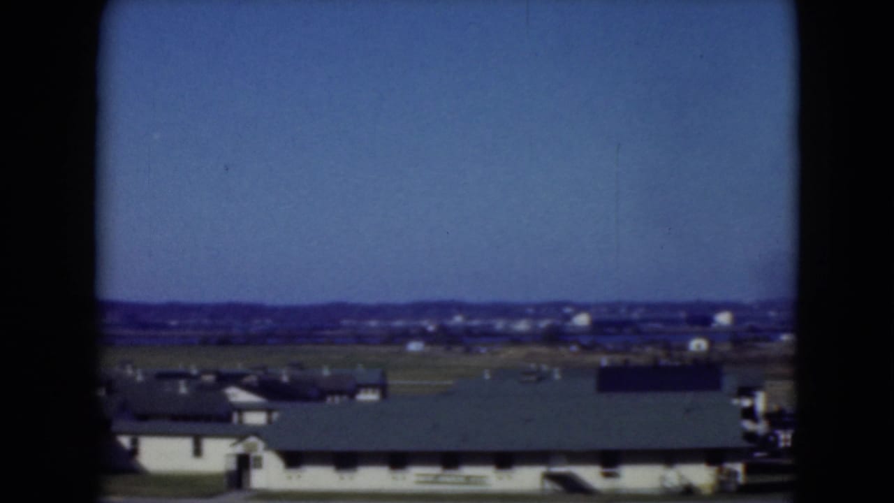 Mid-1970s 8mm view across a quiet Middletown complex with low buildings, open land, and distant structures.
