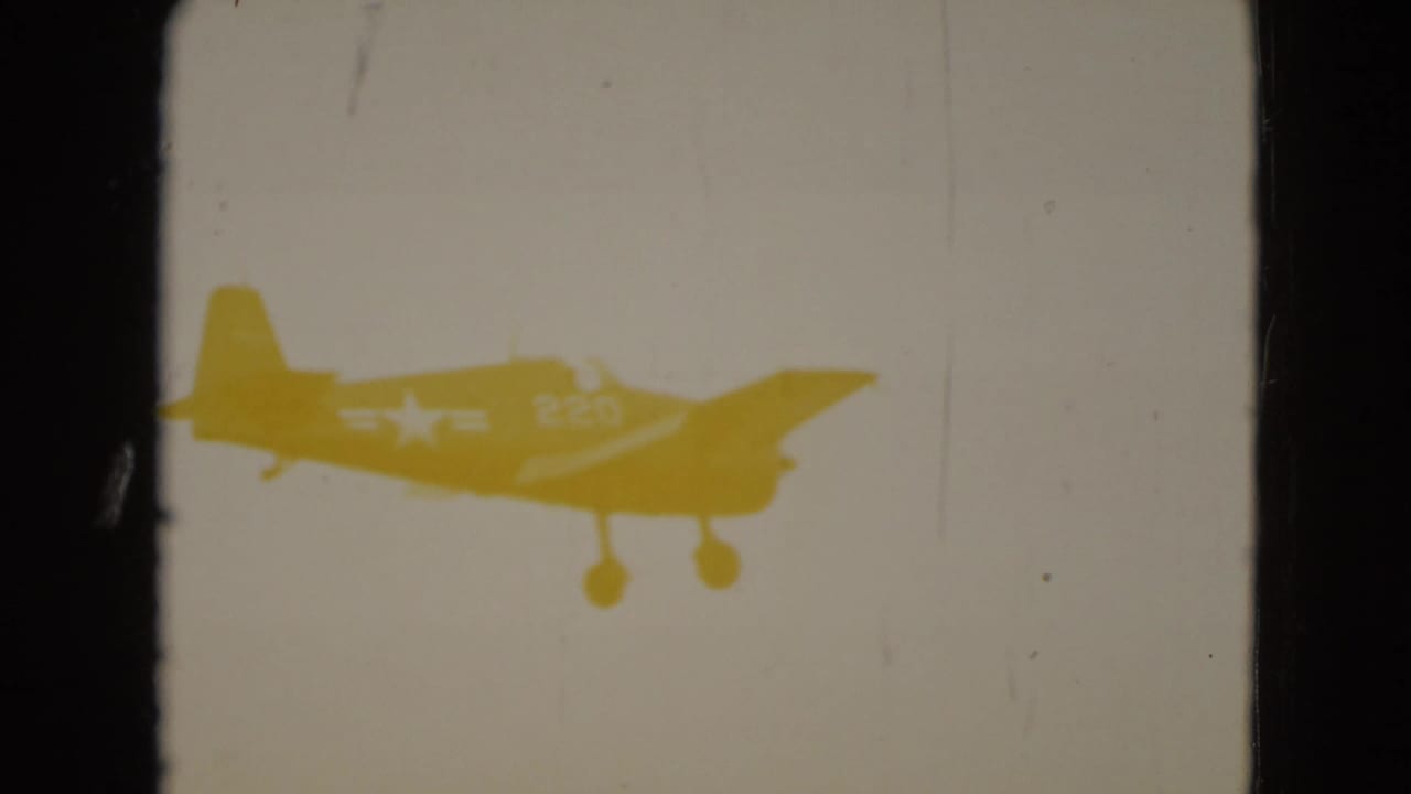 Small propeller airplane in silhouette against a bright, overexposed sky in 1975 8mm home-movie footage.
