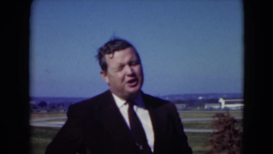 The man in a dark suit turns partly to the side in Middletown, Pennsylvania, with a broad blue sky and rural-suburban landscape behind him.