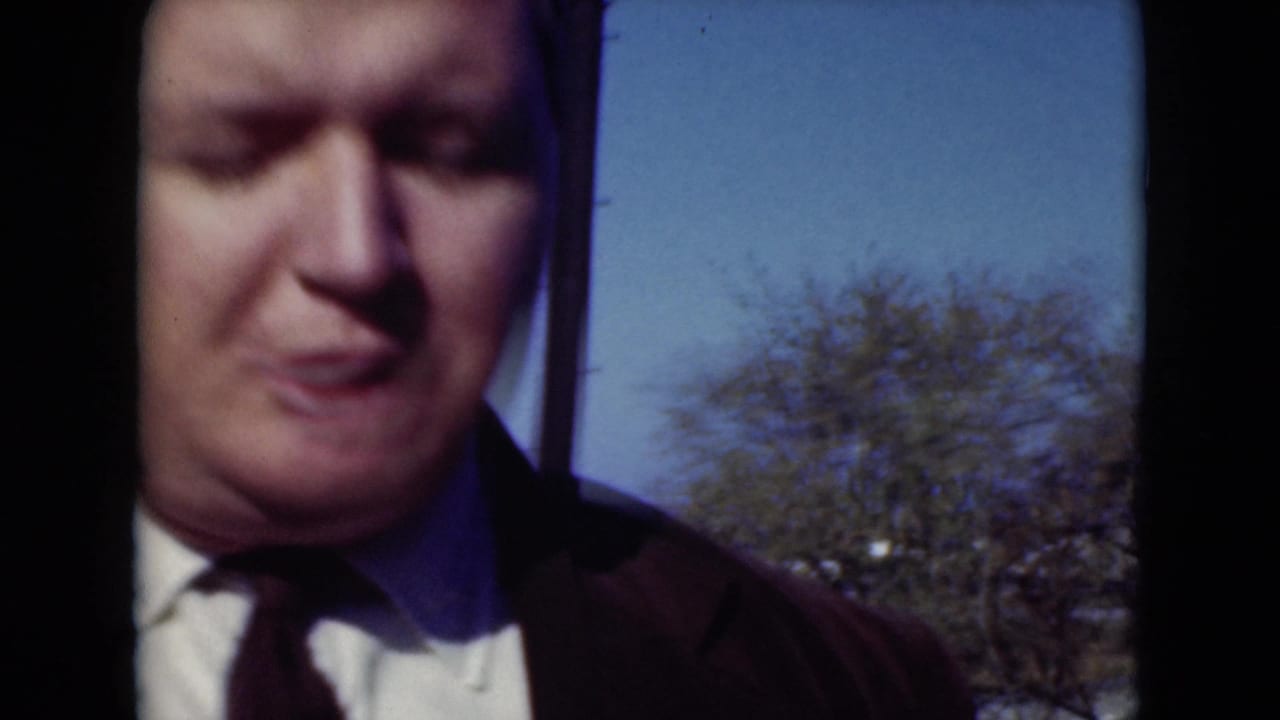 Close 8mm frame of the suited adult man in Middletown, Pennsylvania, with blue sky and a tree visible behind him.