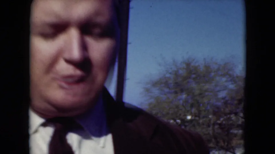 Close 8mm frame of the suited adult man in Middletown, Pennsylvania, with blue sky and a tree visible behind him.