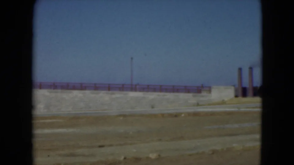 Wide Middletown roadside view showing a concrete wall, red railing, open ground, and distant smokestacks under blue sky.
