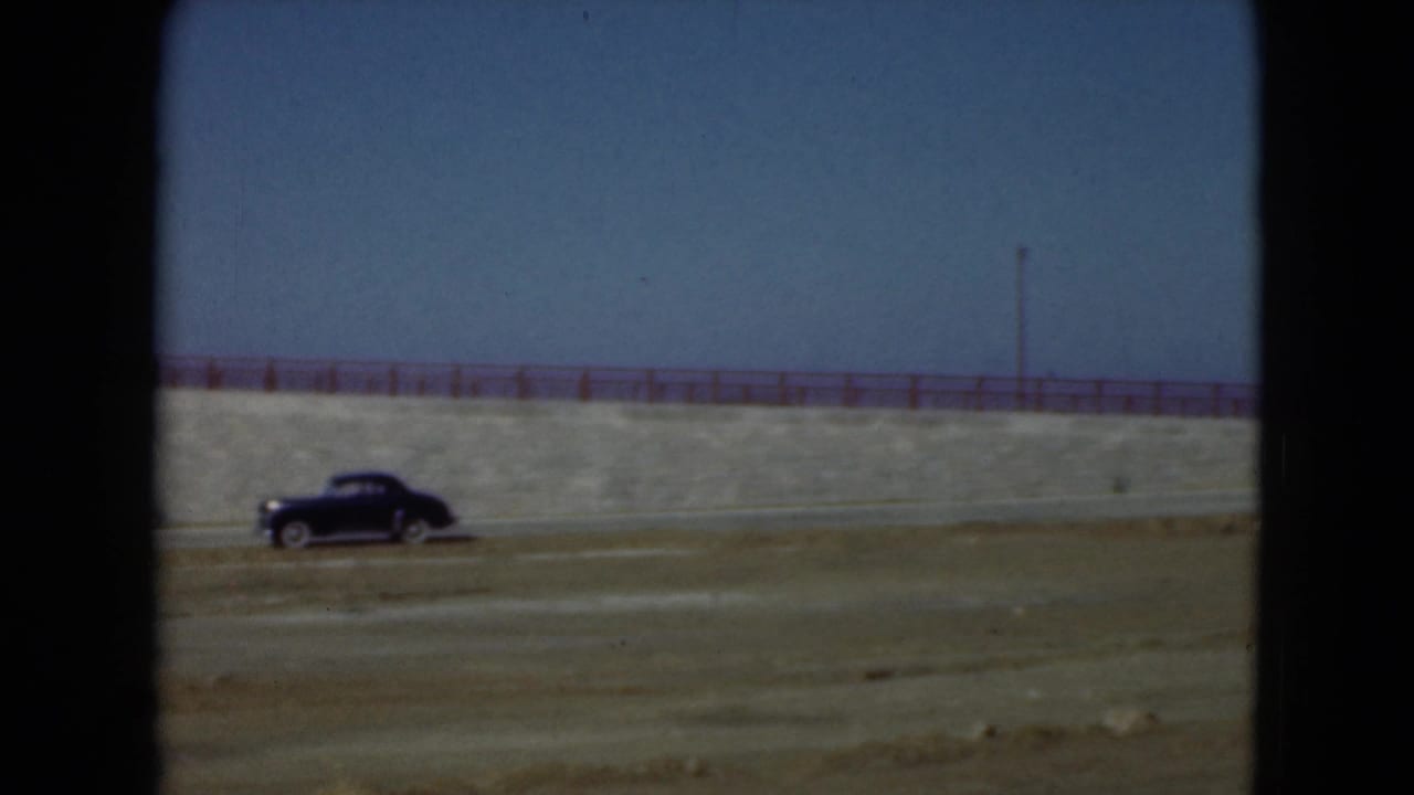 Black vintage car on a road beside a stone embankment with red railing.