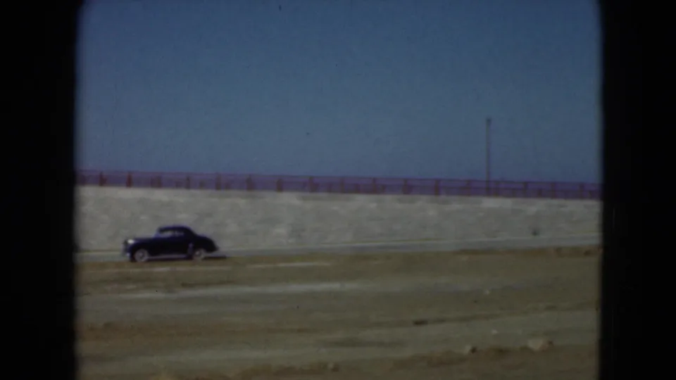 1975 8mm frame from Middletown, Pennsylvania, showing a black rounded car driving beside a stone aqueduct or embankment.