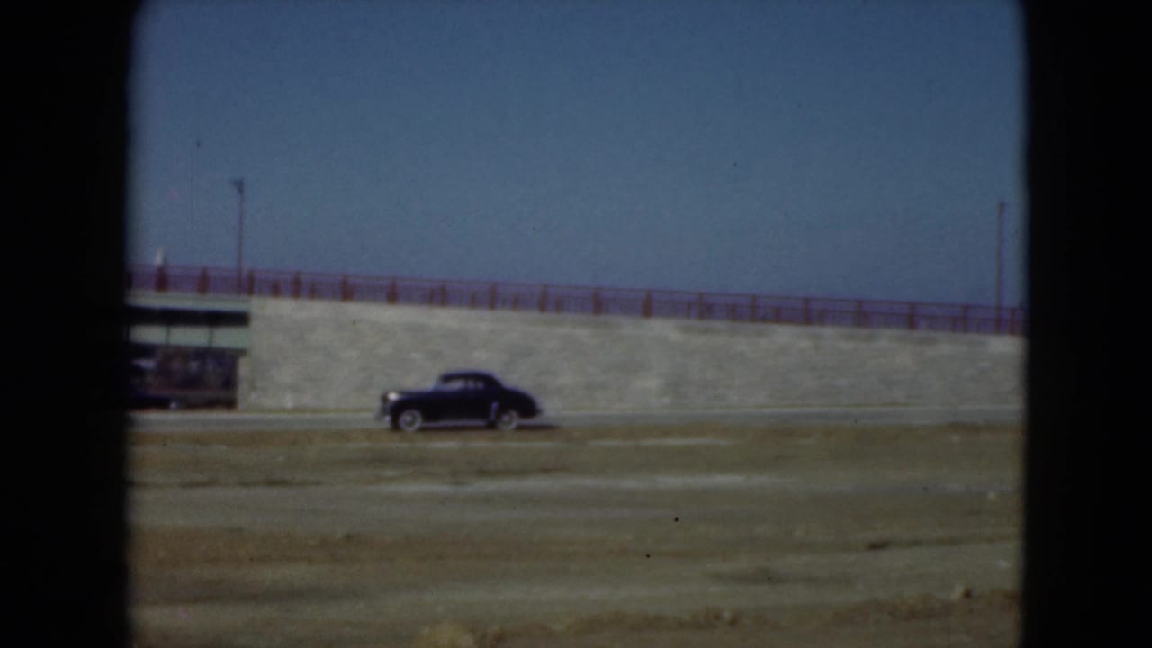 Black car near a roadside structure and stone embankment with red railing.