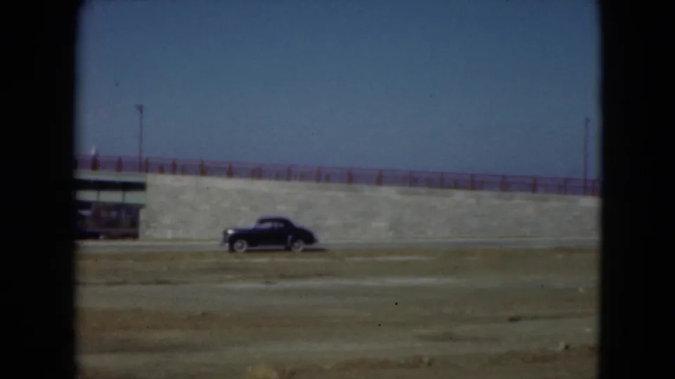 1975 Middletown roadside view with a black vintage car passing a small structure beside a stone aqueduct or embankment.
