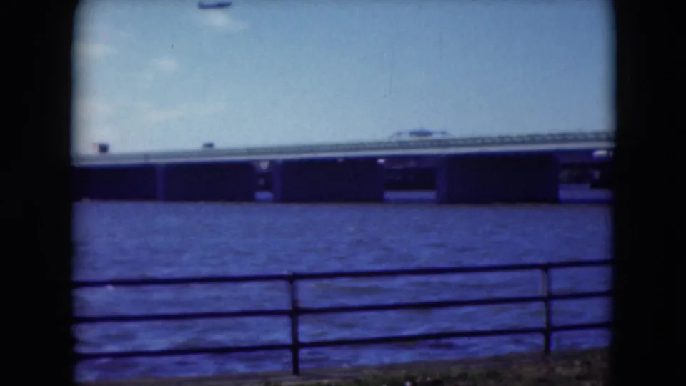 1975 Middletown, Pennsylvania home-movie frame of a river bridge beyond shoreline railings, with blue-tinted film color.