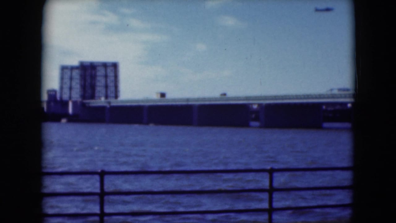 1975 Middletown, Pennsylvania, home-movie frame with a bridge, blue water, railing, and large industrial building across the river.