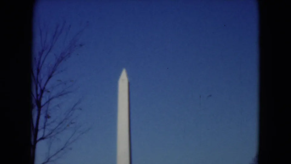 1975 8mm travel frame showing the Washington Monument in the distance, with bare tree branches at the left edge.