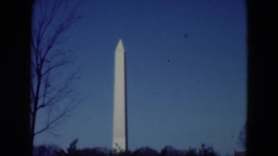 1975 8mm frame with the Washington Monument centered in a clear sky above a low dark treeline.