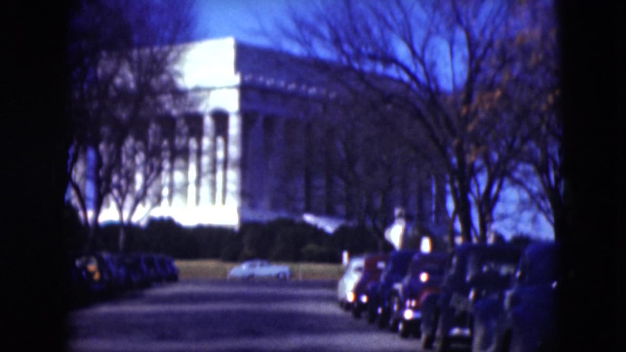 1975 Middletown-area 8mm frame showing a drive toward a large white columned building, with parked cars and bare trees along the road.