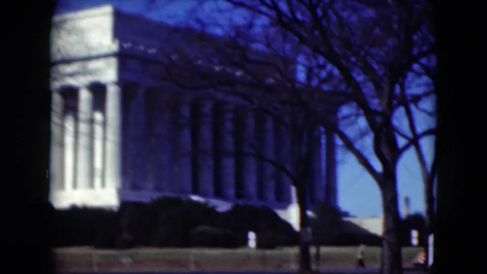 Near the end of the clip, the white columned building dominates the frame while bare trees and shrubs partially obscure the facade.