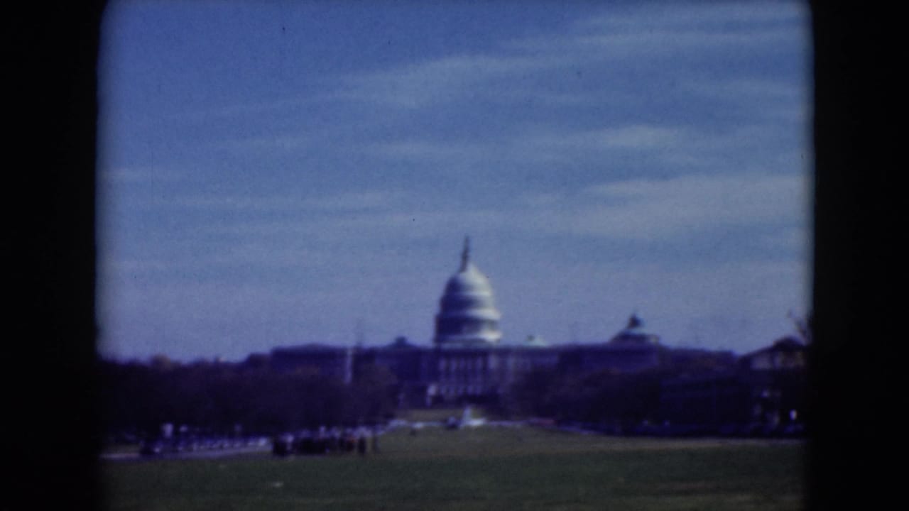 1975 8mm visitor view of the U.S. Capitol dome seen across the National Mall lawn under a blue sky.