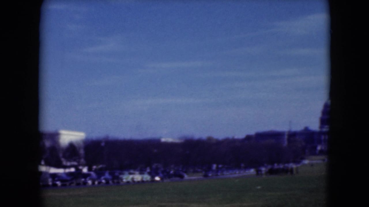 1975 8mm view across the National Mall with a white classical landmark, traffic, trees, and distant visitors.