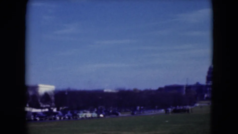 1975 8mm view across the National Mall with a white classical landmark, traffic, trees, and distant visitors.