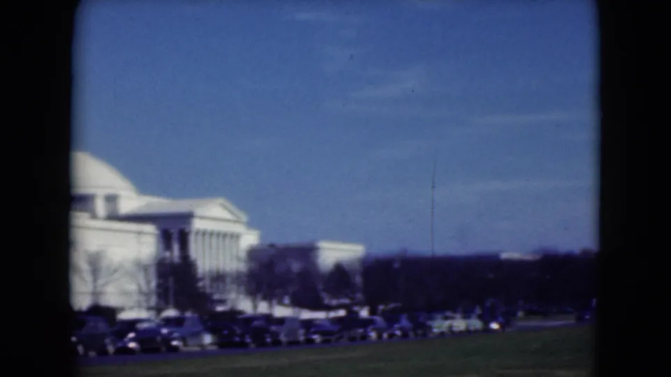 1975 8mm Washington DC landmark view showing a white columned building, roadside cars, trees, and film gate borders.