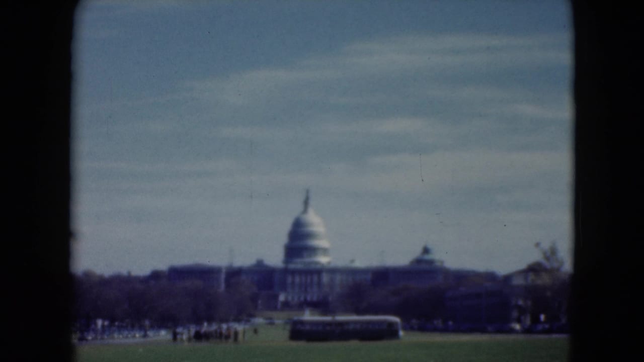 1975 8mm view toward the U.S. Capitol in Washington, D.C., framed by dark film borders with visitors and a bus on the lawn.