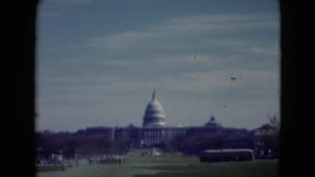 1975 8mm view toward the U.S. Capitol in Washington, D.C., with lawn, road traffic, and dark window or doorway edges in the foreground.