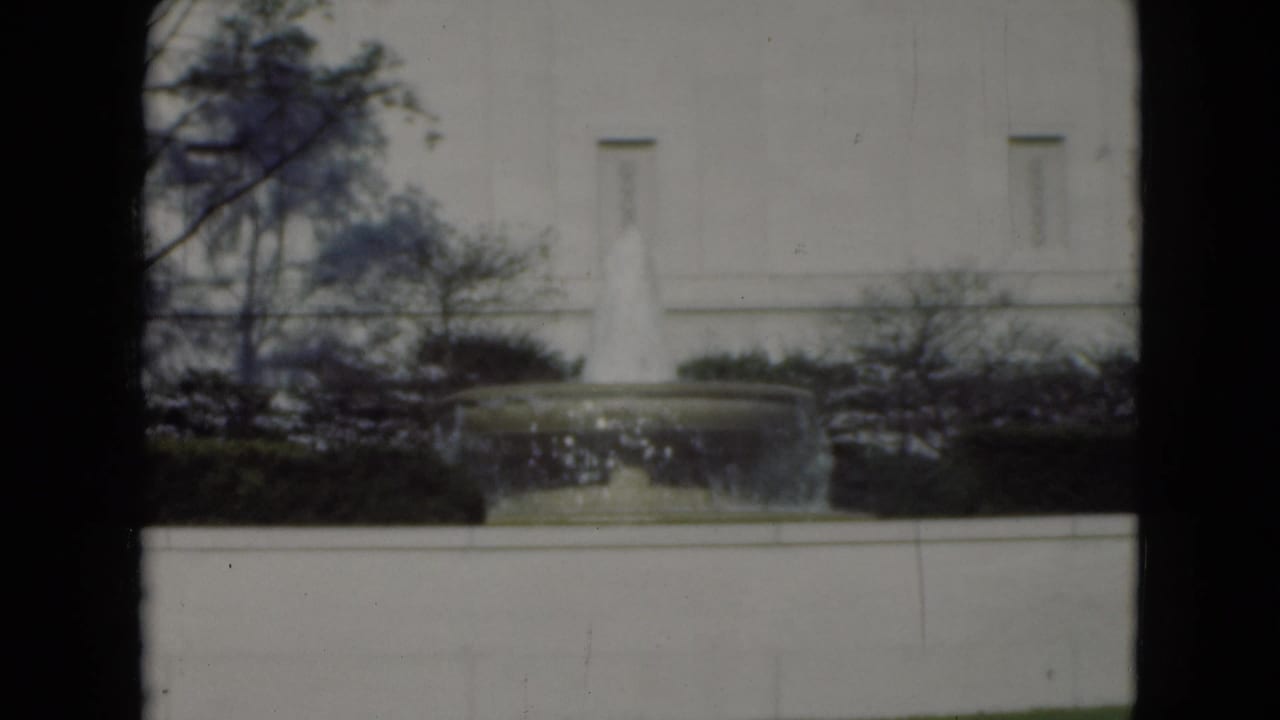 1975 Middletown, Pennsylvania 8mm frame showing a circular fountain before a pale building, bordered by hedges and bare tree branches.
