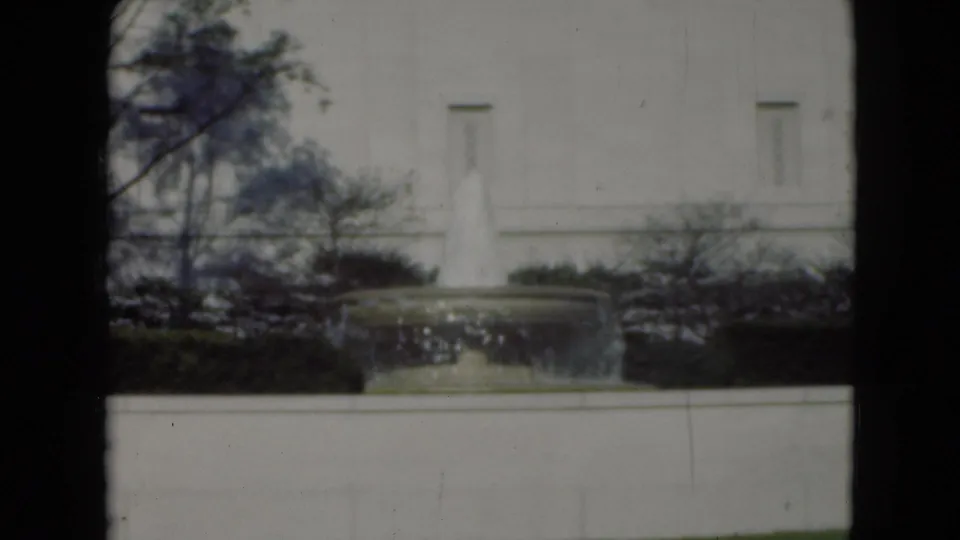 1975 Middletown, Pennsylvania 8mm frame showing a circular fountain before a pale building, bordered by hedges and bare tree branches.