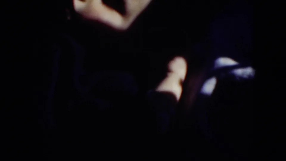 A dark, close 8mm frame shows a bright limb and dark clothing or objects near the camera after the exterior fountain view.