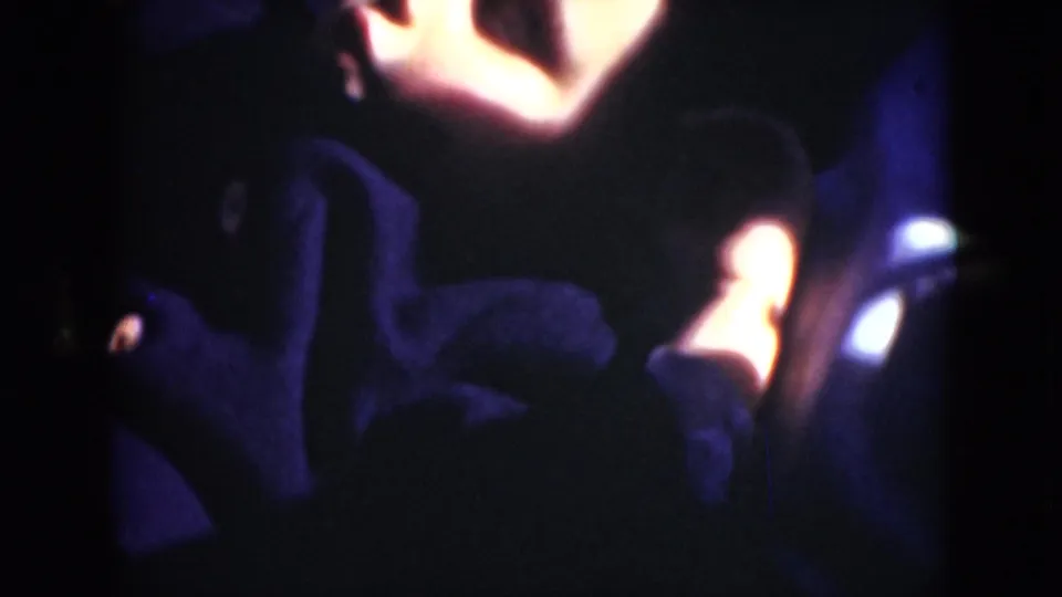 A dim final 8mm frame shows dark clothing, a bright limb near the top edge and a small reflective object near the side of the view.