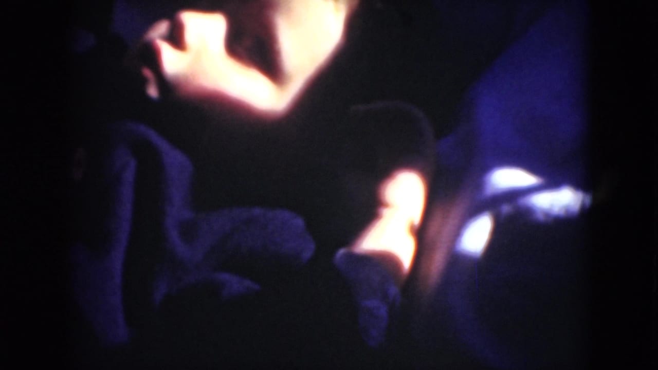 A dim 8mm interior frame shows a reclining person mostly obscured by shadow, with bright warm and white highlights at the edges.