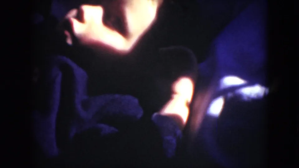 A dim 8mm interior frame shows a reclining person mostly obscured by shadow, with bright warm and white highlights at the edges.