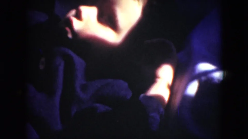 Metadata-supported 1975 home-movie frame with a shadowed reclining person, warm light on the upper body, and dense 8mm grain.