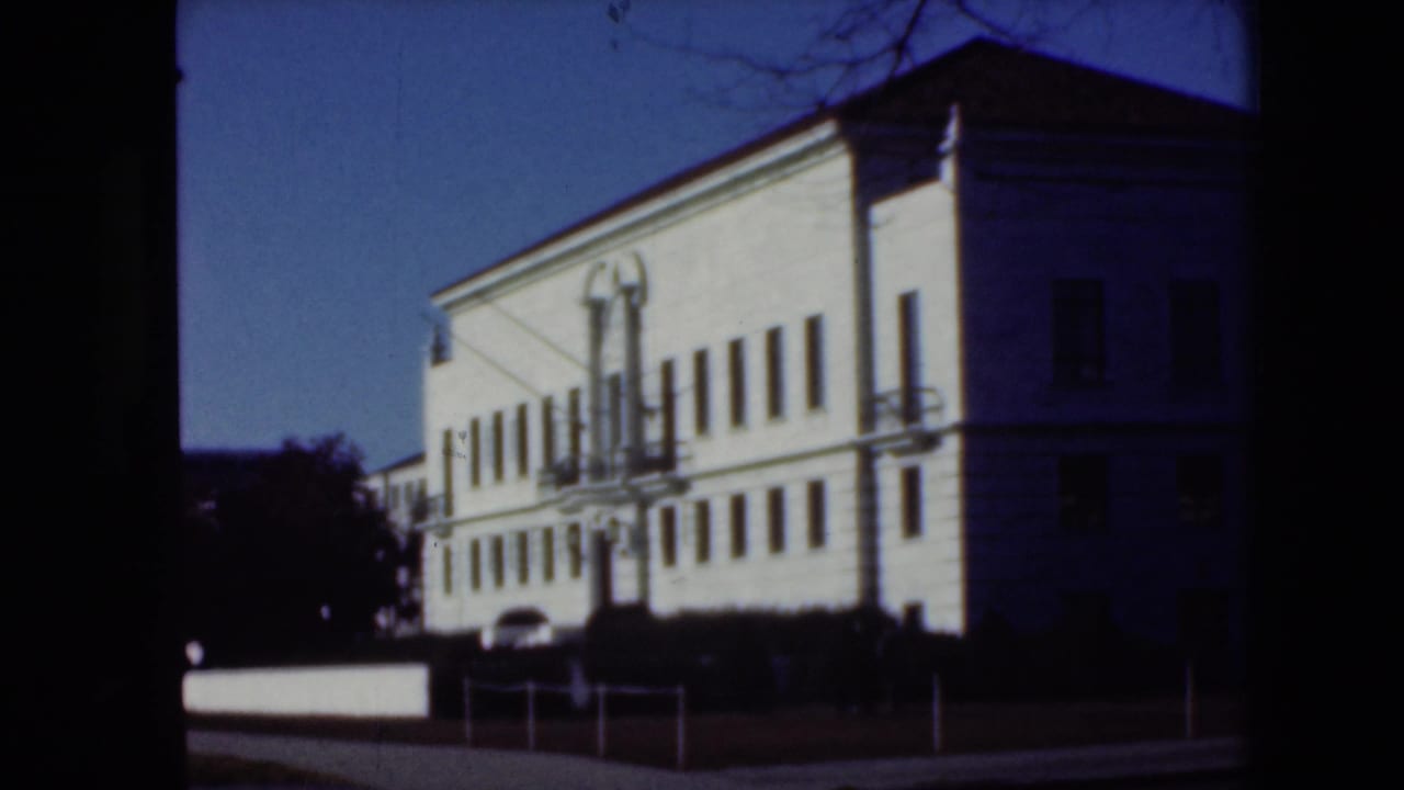 Similar street view of the white building, with railings, shrubs, and a dark vertical film edge.
