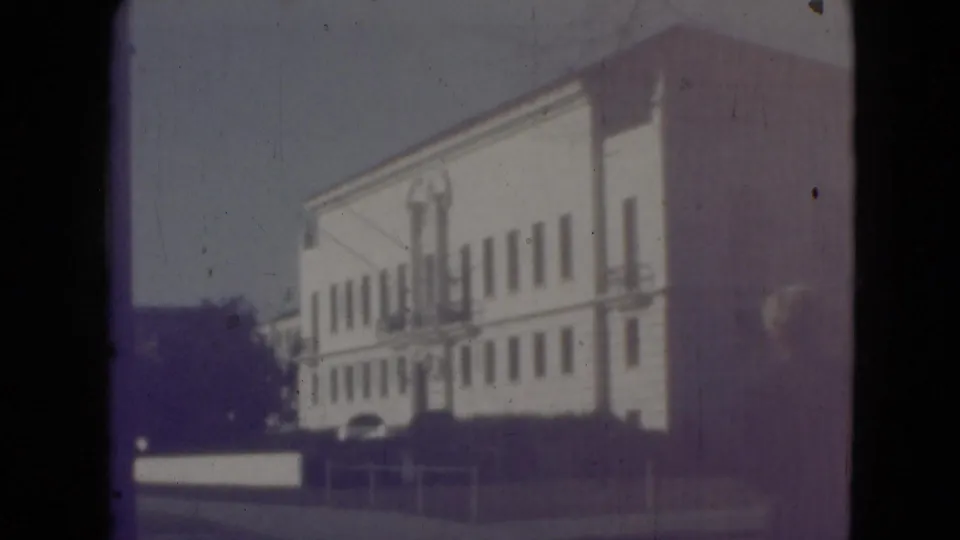 Faded 8mm frame from the Middletown exterior sequence showing the white building through exposure flare and film aging artifacts.