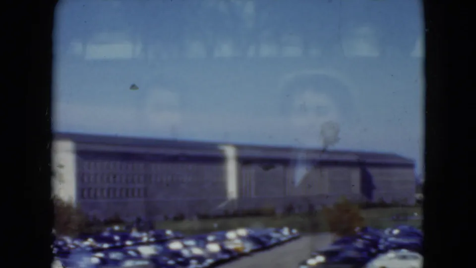 Wider 1975 8mm view in Middletown, Pennsylvania showing a long institutional building beyond a parking lot filled with cars.