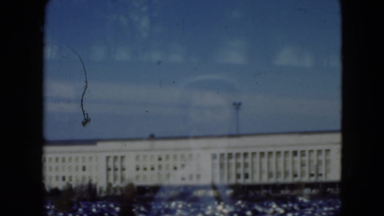 Distant white building and parked cars viewed through a window with a central dark mullion.