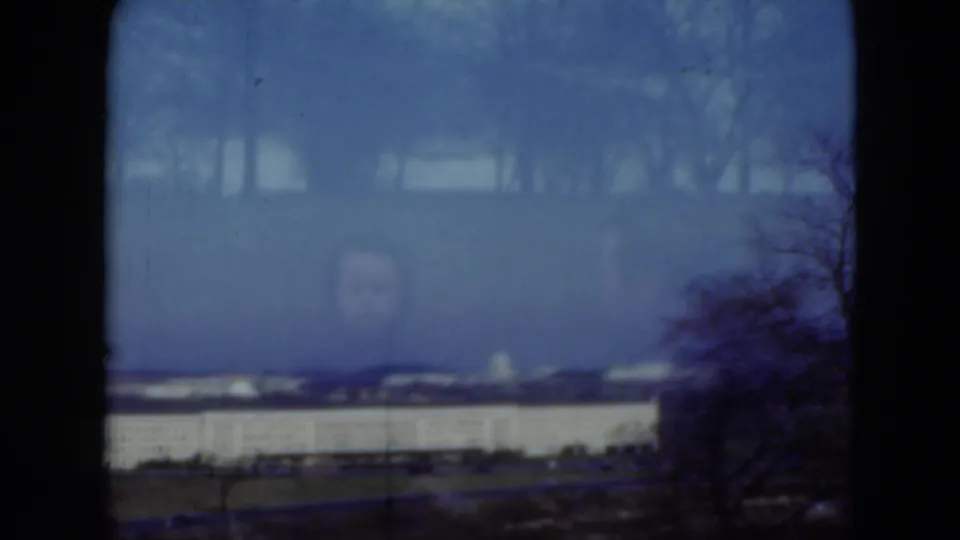 The final 1975 Middletown frame shows a distant institutional building through glass, with tree branches and a faint face-like reflection on the pane.