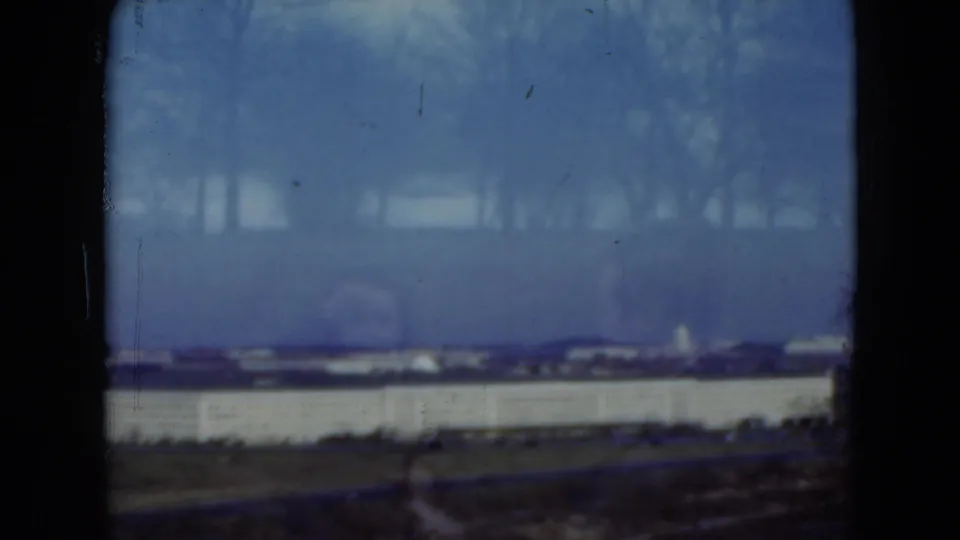 1975 Middletown-area frame with a long pale building, distant rooflines, bare trees, and visible 8mm film wear.