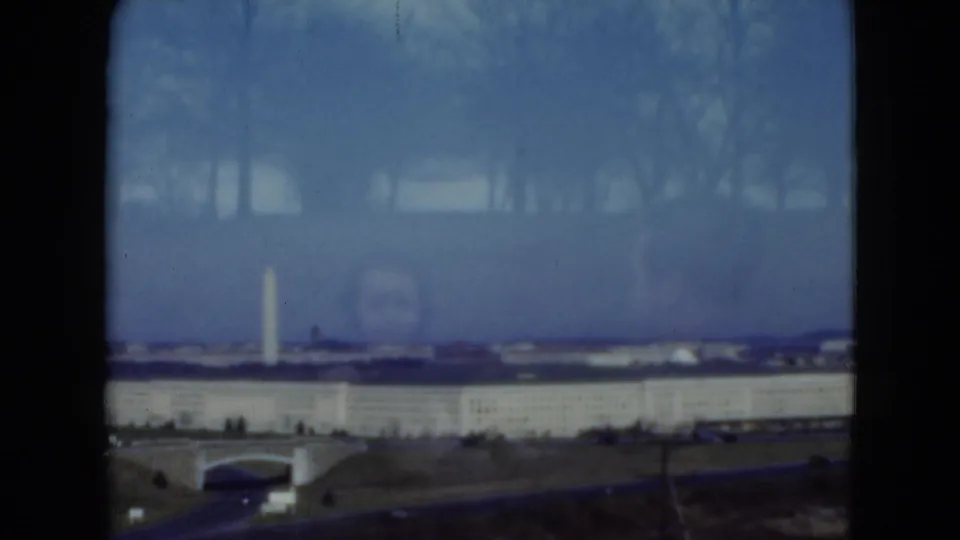 1975 Middletown-area roadside view with grass, low structures, a long pale building, and a distant vertical landmark-like form.