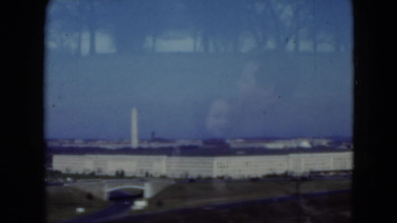 1975 8mm frame showing a distant Pentagon and Washington Monument view through a vehicle window, with blue sky and reflections.
