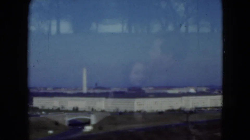 1975 8mm frame showing a distant Pentagon and Washington Monument view through a vehicle window, with blue sky and reflections.